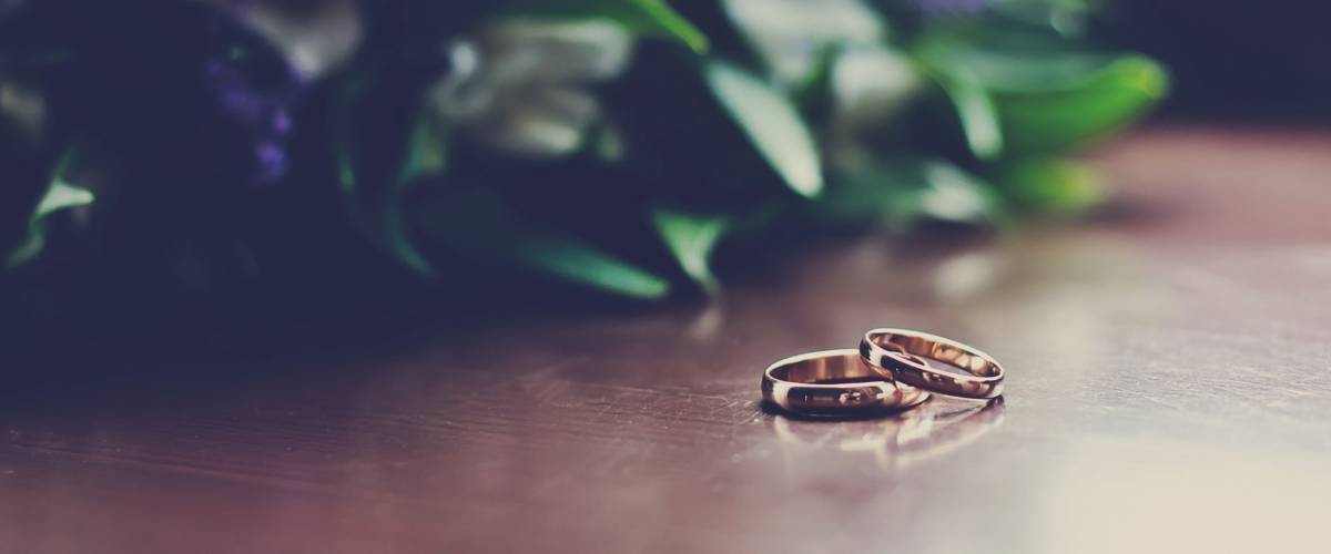 Beautiful toned picture with wedding rings lie on a wooden surface against the background of a bouquet of flowers