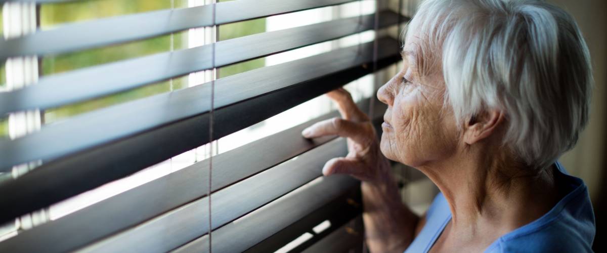Senior woman looking out from window blind at home