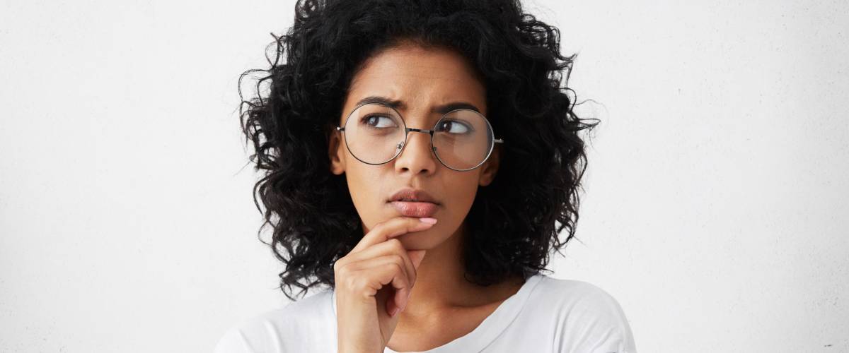 Isolated portrait of stylish young mixed race woman with dark shaggy hair touching her chin and looking sideways to make a decision