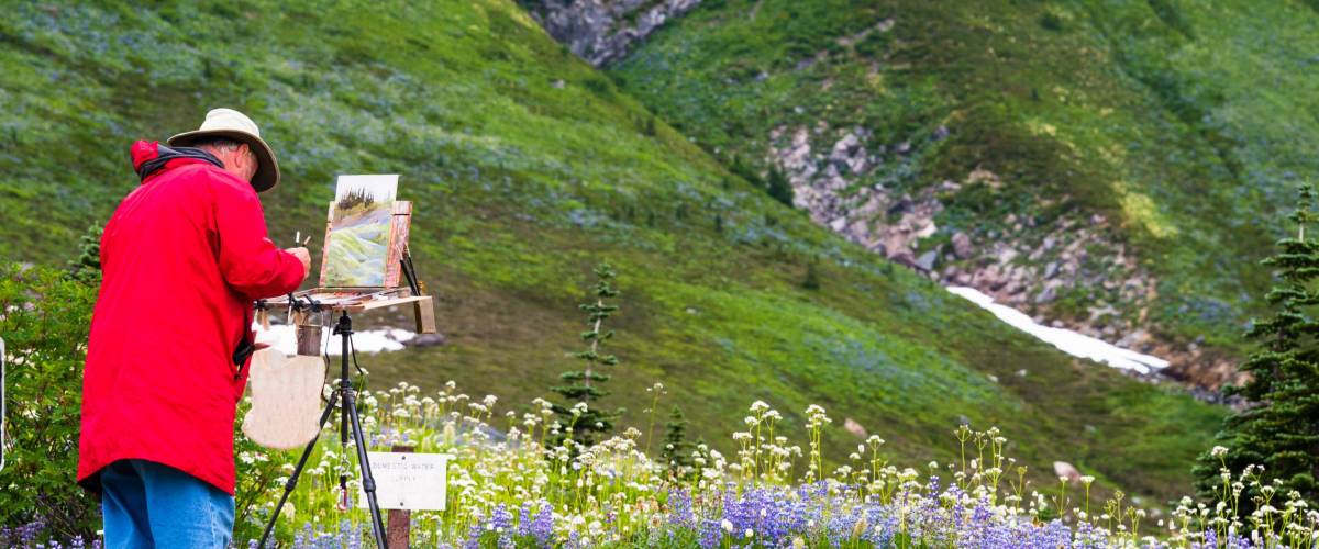 Artist outside in the field painting on his easel a landscape of the wildflowers in the mountains. Copy space.