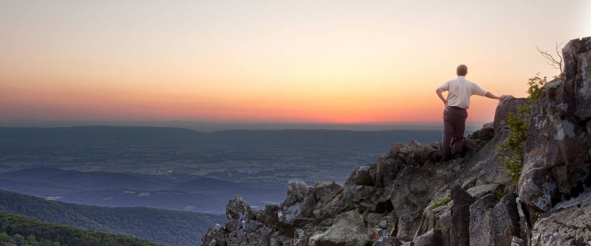 Back view of man watching sunset from rocky summit of Stony Man on Skyline Drive in Virginia
