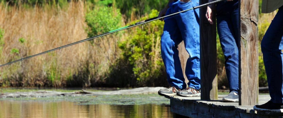 Three fishermen stand on a wooden dock over a lake. They are bream fishing. Photo shows only their legs and shoes.