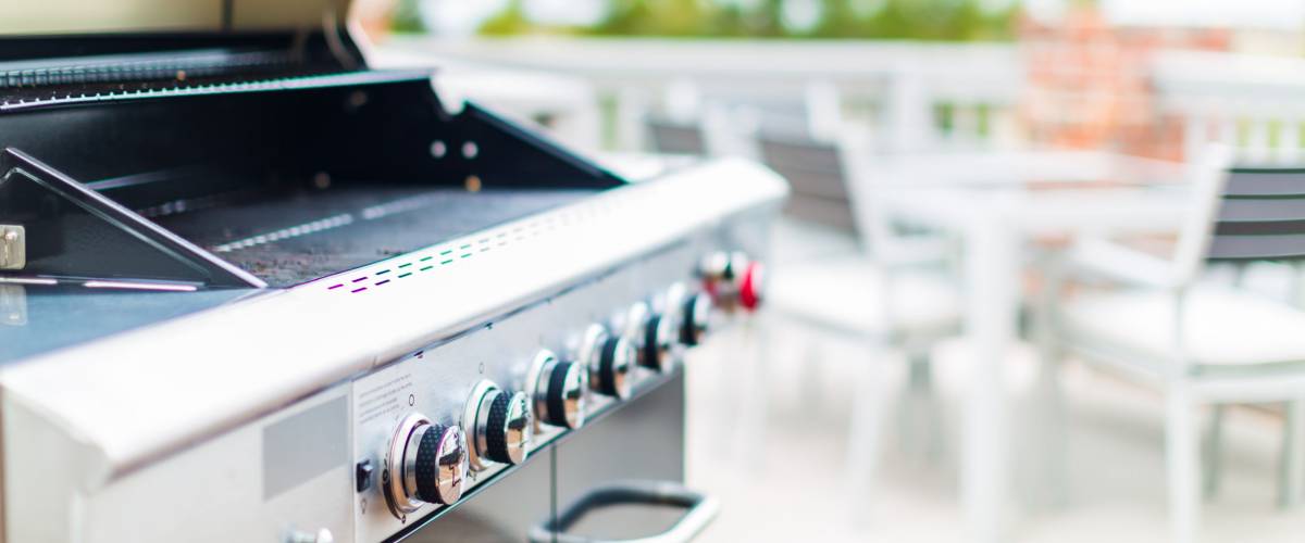 Six burner outdoor gas grill with open lid on backyard.