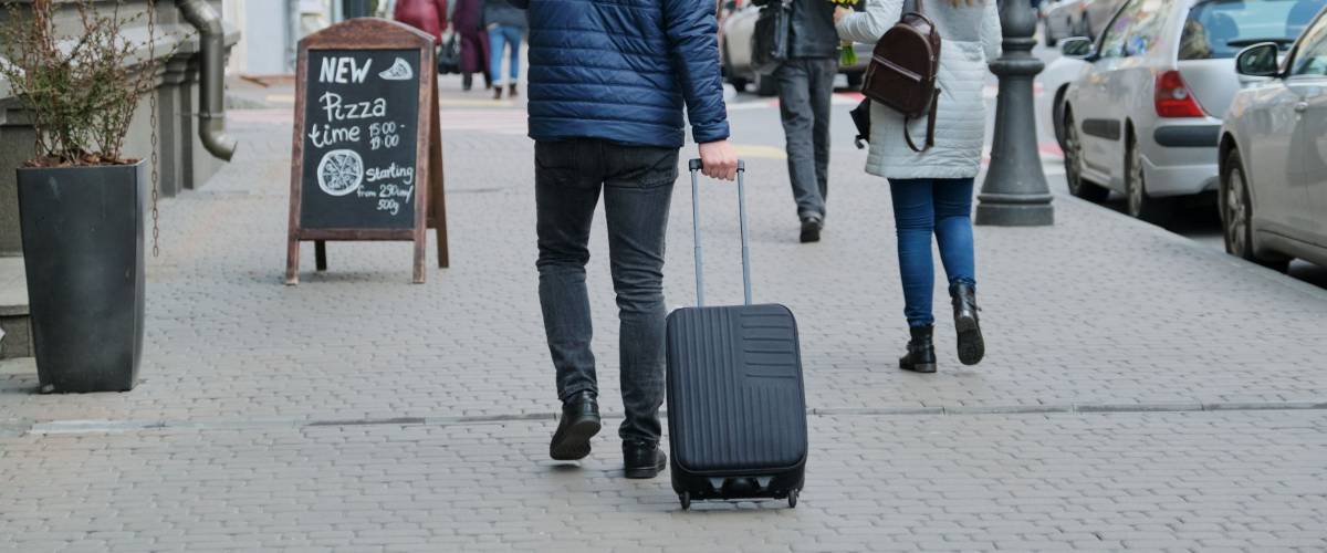 Man in jacket with suitcase walking down city street, back view.