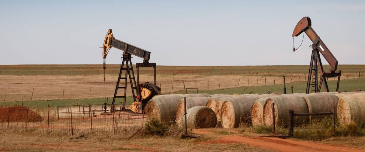 A scene from rural Oklahoma. Oil pumps and hay bales in the prairie.