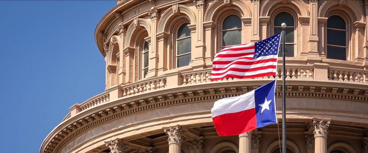 American and Texas state flags flying on the dome of the Texas State Capitol building in Austin