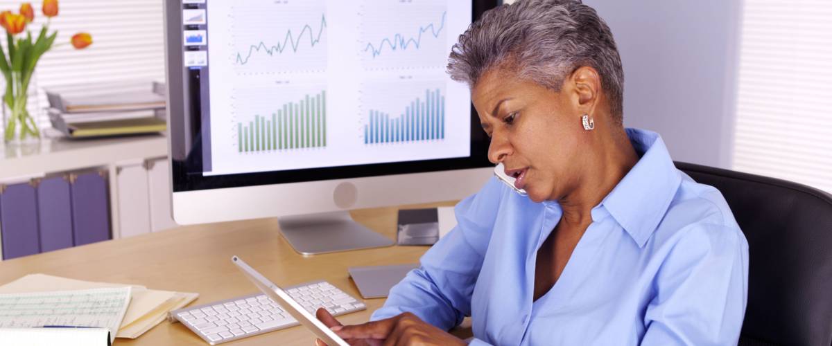 Senior black businesswoman talking on smartphone and using tablet