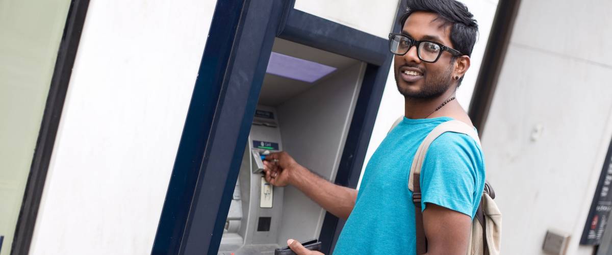 young indian man at the cashpoint withdrawing money