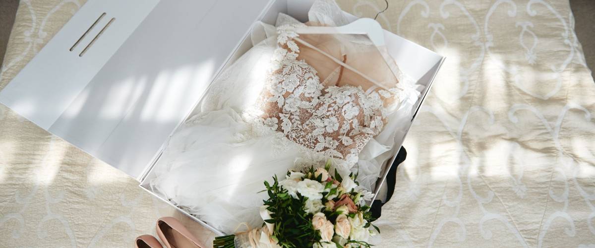 Luxury wedding dress in white box, beige women's shoes and bridal bouquet on bed, copy space. Bridal morning preparations. Wedding concept