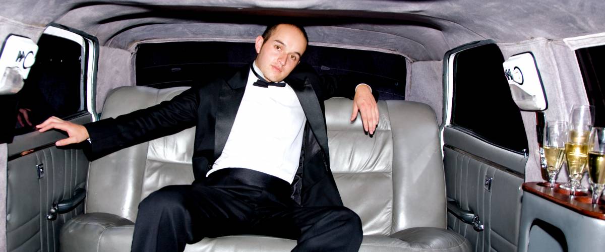 Young man in a tuxedo in a limousine with champagne