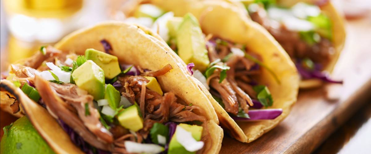 three pork carnitas street tacos in yellow corn tortilla with avocado, onion, cilantro and cabbage