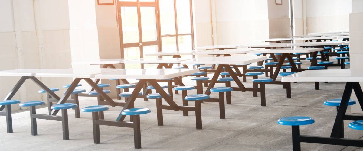 Clean school cafeteria with many empty seats and tables.