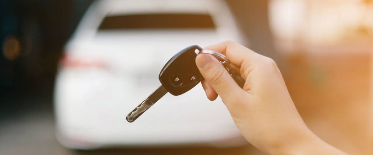 Female holding car keys with car on background.