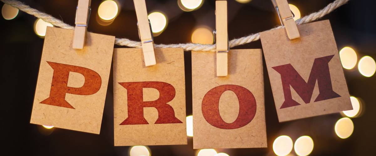 The word PROM printed on clothespin clipped cards in front of defocused glowing lights.