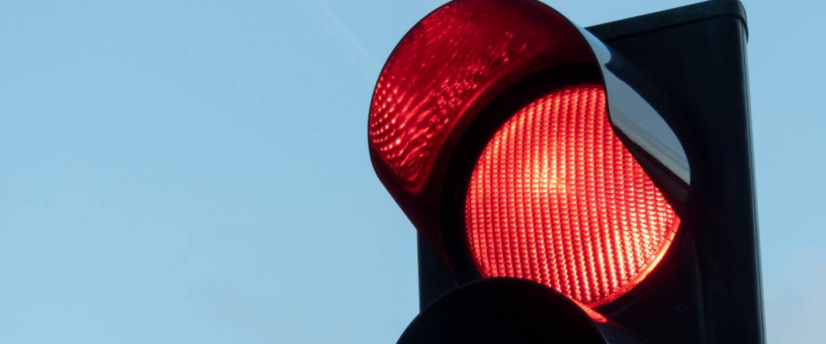 Red signal on traffic light in focus and blue sky in the background.