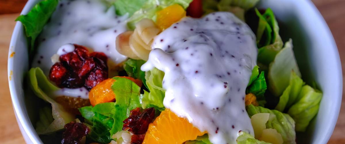 Green salad with mandarin oranges, almonds and poppyseed dressing in white bowl on white cutting board