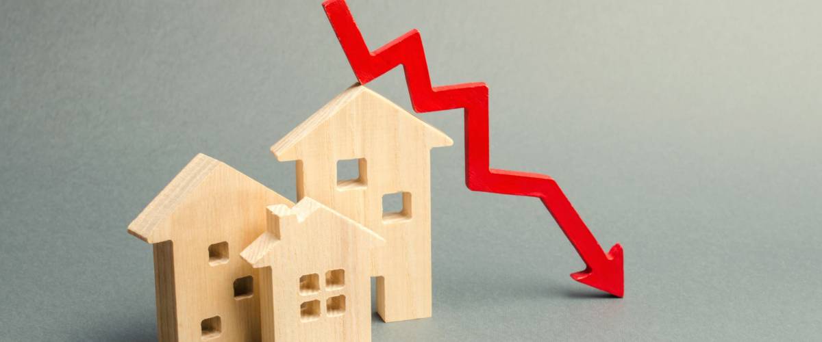 Miniature wooden houses and a red arrow down.Falling interest rates