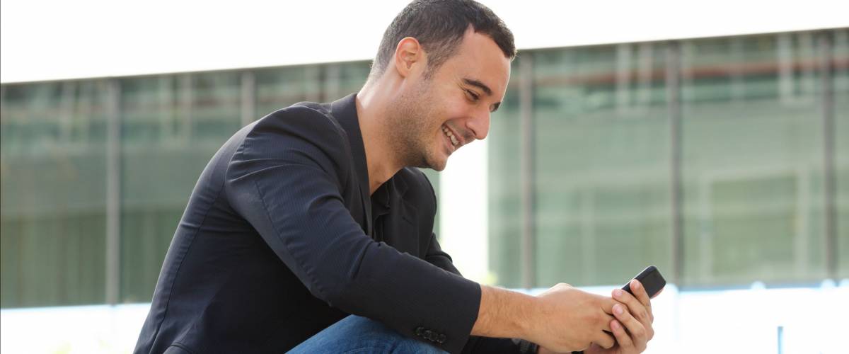 Portrait of smiling man sitting outside and looking at mobile phone