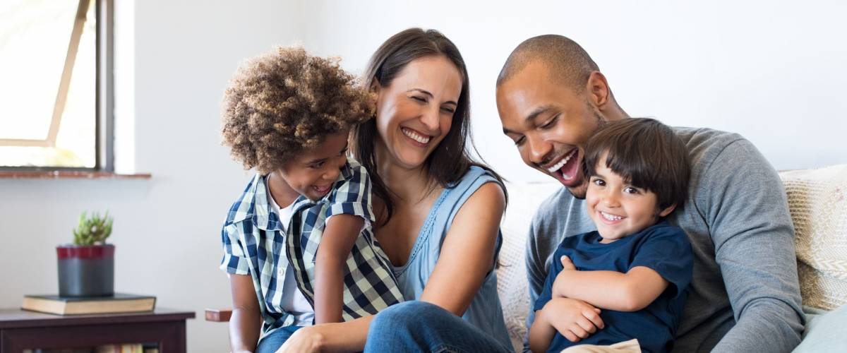 Happy multiethnic family sitting on sofa laughing together.