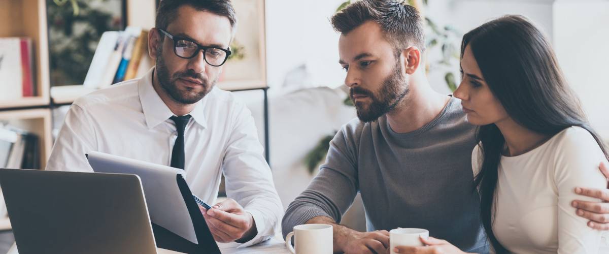 Salesman sitting together with young couple at the desk in office