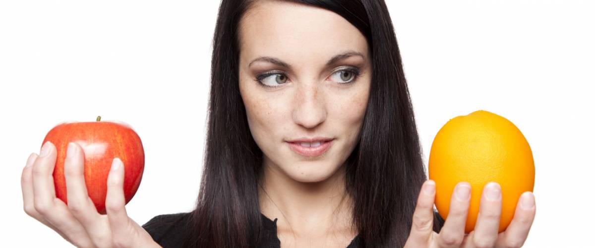 Isolated studio shot of a dark haired caucasian woman comparing apples to oranges.