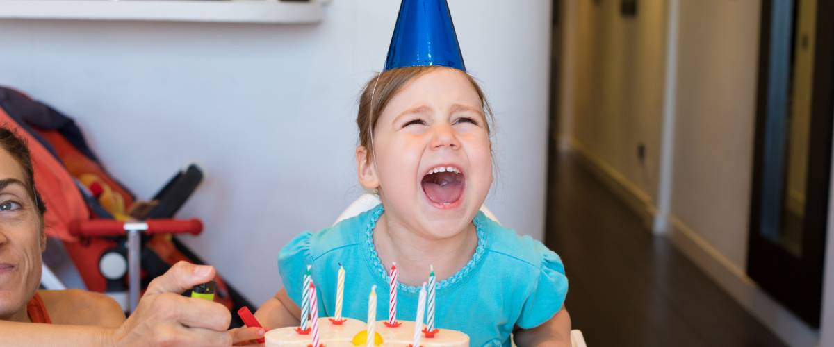 three years old blonde child with blue shirt and cone hat, and birthday cake