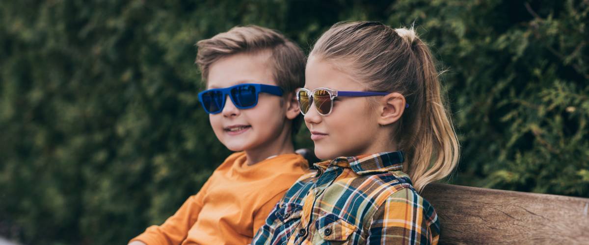 stylish little kids in sunglasses sitting on bench at park