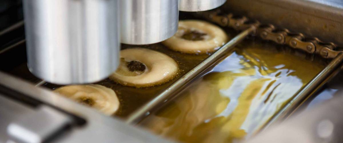 Mini-donut machine. Automatic donuts conveyor. Frying hot dessert. Three doughnuts dispenser photo. Close up photo.