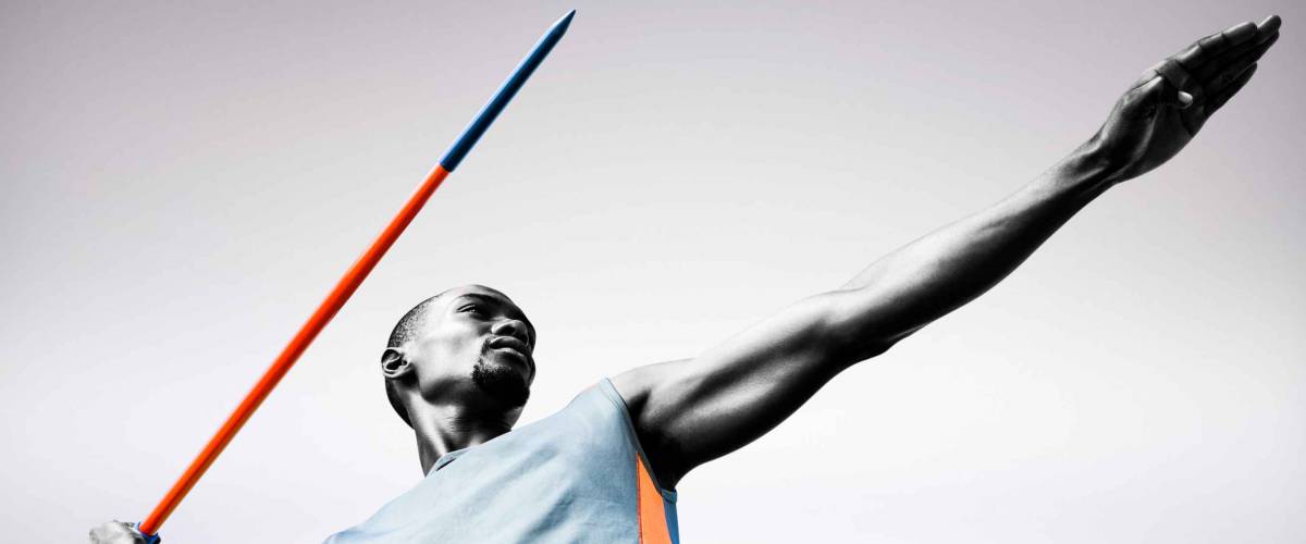 Low angle view of sportsman practising javelin throw against grey background