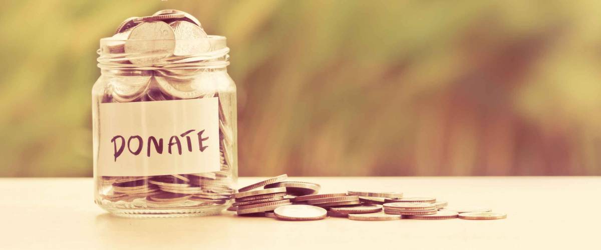 Hand putting Coins in glass jar with DONATE word written text label for giving and donation concept