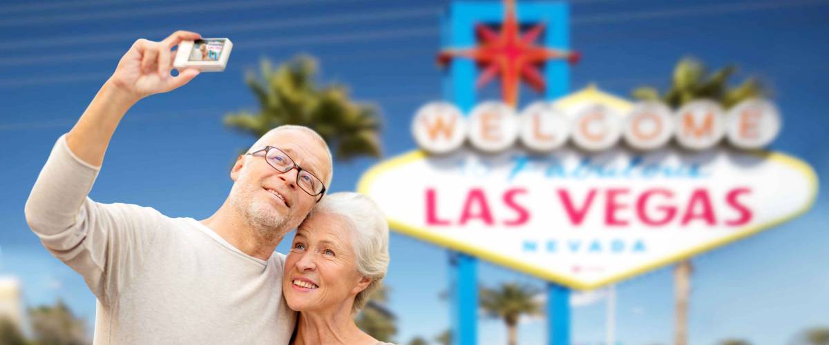 vacation, tourism and travel concept - happy senior couple hugging and taking photo by digital camera over welcome to fabulous las vegas sign background