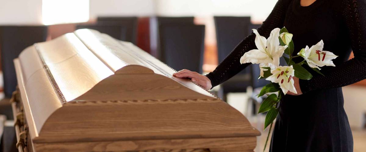 people and mourning concept - woman with white lily flowers and coffin at funeral in church