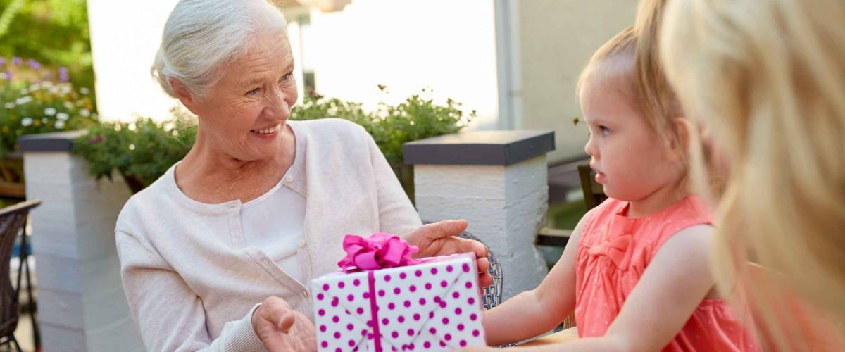 grandmother handing a wrapped present to granddaughter