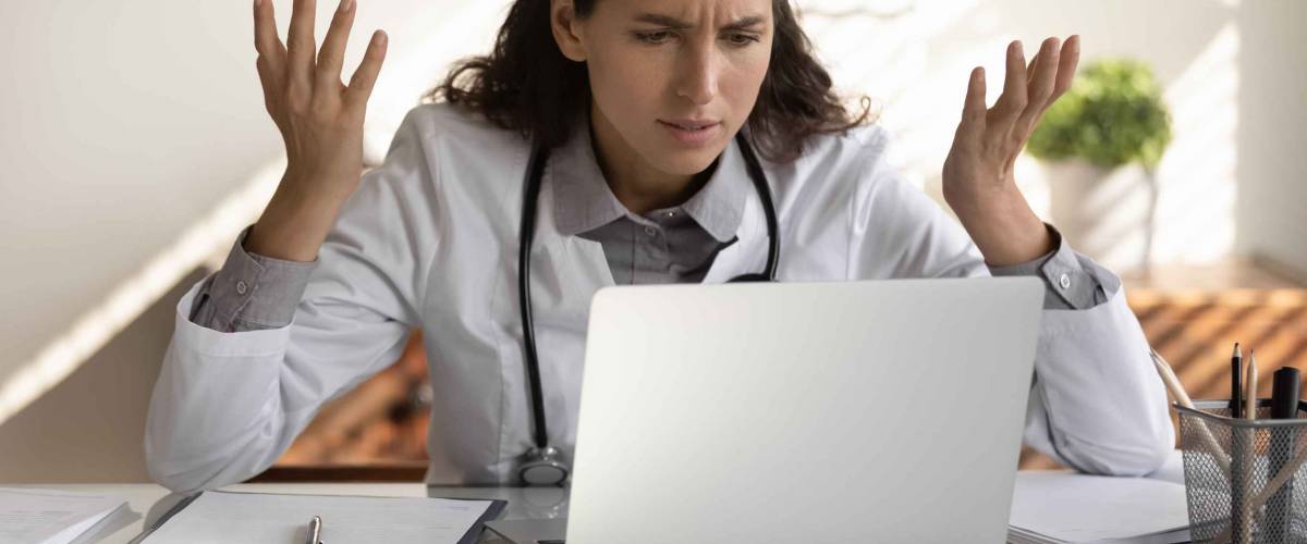 Female nurse or doctor looking at her laptop in clinic, looking frustrated and confused