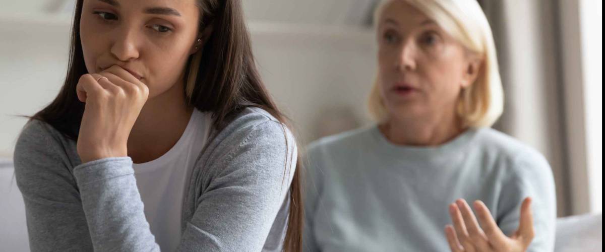 Focus on young woman sitting with elderly mother-in-law behind her telling her something she doesn't want to hear