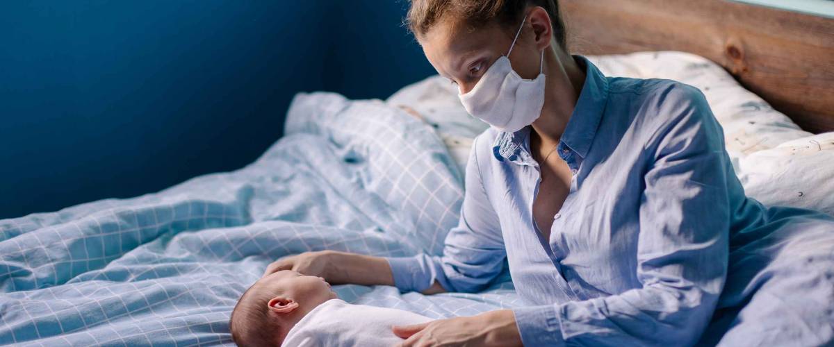 young mother wearing a protective face mask, holding her baby