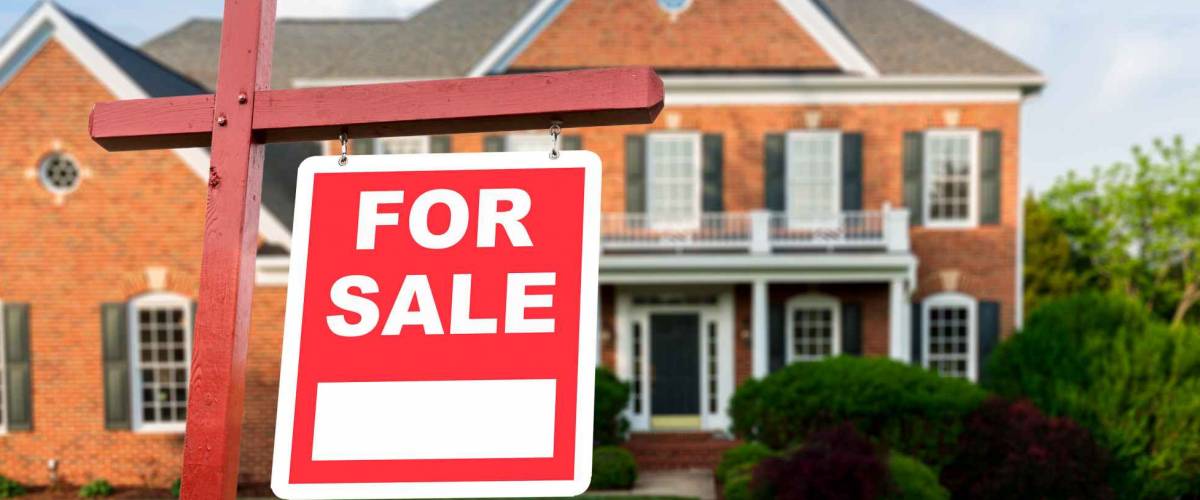 For Sale realtor sign in front of large brick single family house in expansive grass yard for real estate opportunity