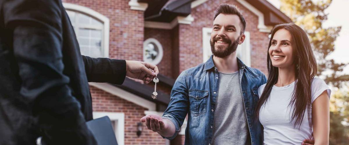 Happy couple is taking keys from their new house from broker and smiling.