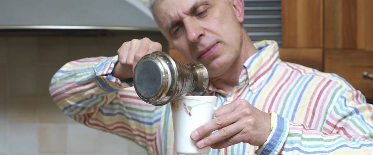 Man carefully pouring hot fresh coffee from a coffee maker into a cup, kitchen interior in the blurred background