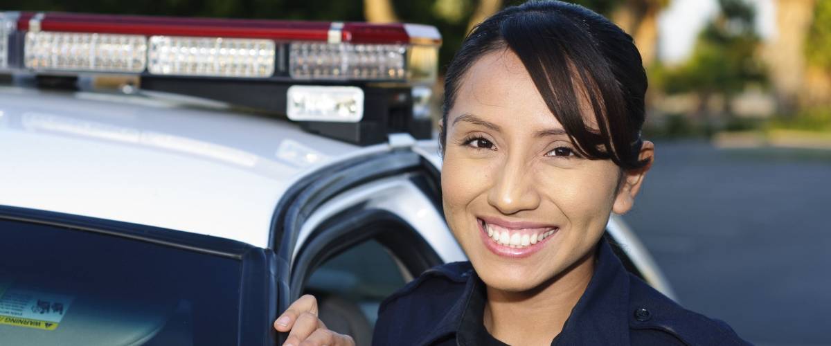 a smiling Hispanic police officer next to her patrol car.