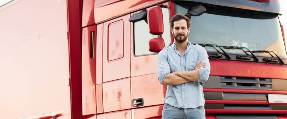 handsome masculine truck driver standing outside with his vehicle behind with folded arms