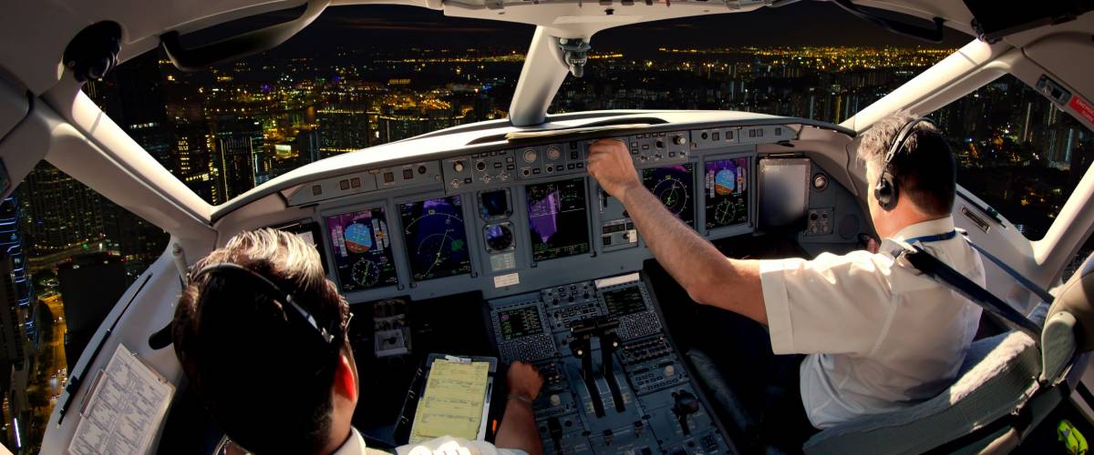 Flight Deck of modern passenger jet aircraft. Pilots at work. Night city view from the plane cockpit.