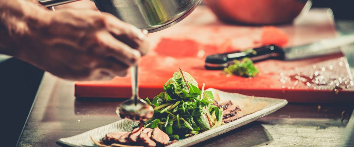 Chef finishing her plate and almost ready to serve at the table. Only hands. Finally dish dressing: steak meat with green salad