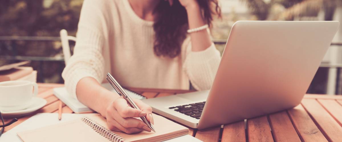 Woman working on computer and writing down her thoughts