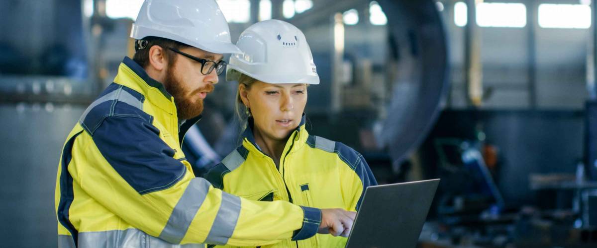 Male and Female Industrial Engineers in Hard Hats Discuss New Project while Using Laptop.