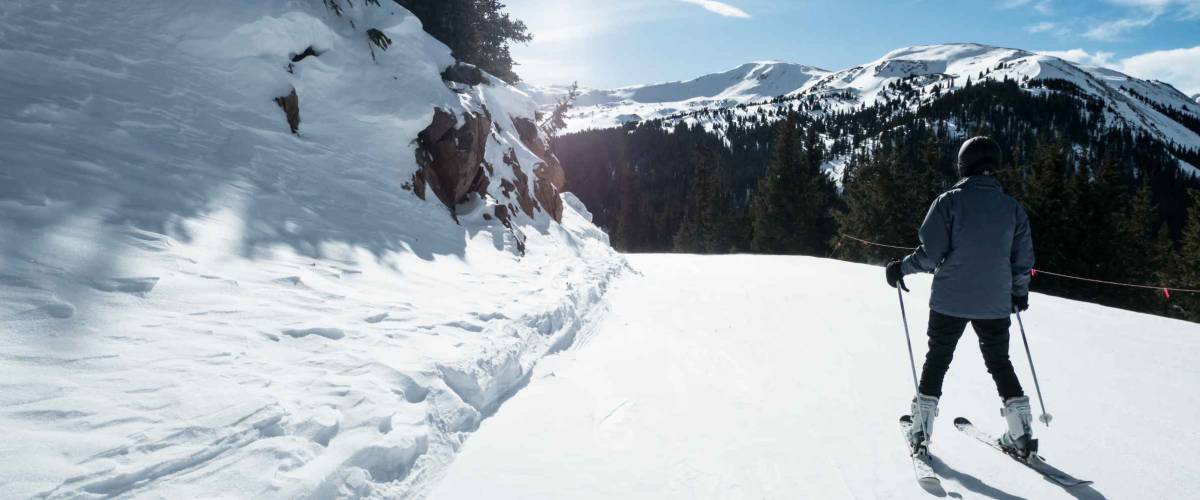 SKIER WITH NICE VIEW OF SKI TRIAL AND PINE TREES IN COLORADO IN BRIGHT BLUE SKY