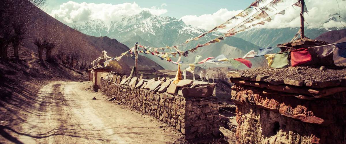 Muntra flag on the stone wall along the pathway to the misty mountain at distance. Annapurna Conservation Area, Nepal, Retro vintage style