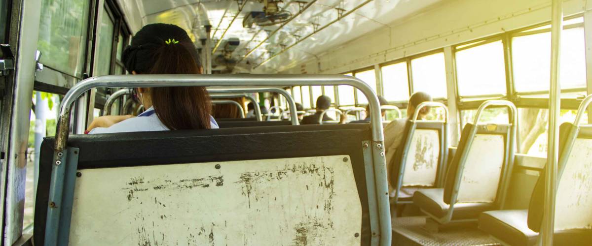 Within the old Thailand Bangkok bus in the morning. there is light in the sun. and there are women in uniform sitting on a chair full of wrinkles. by next to the bus window to travel to work.