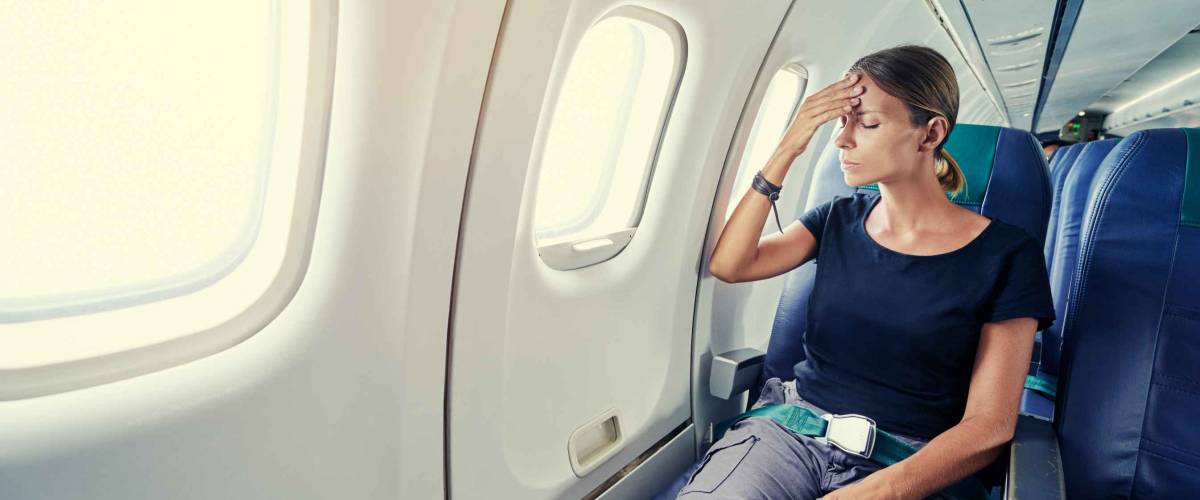 Fear of flying woman in plane airsick with stress headache and motion sickness or airsickness. Person in airplane with aerophobia scared of flying being afraid while sitting in airplane seat.