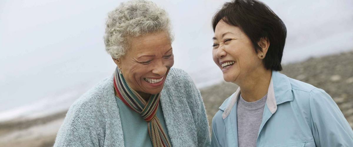 Two cheerful middle aged female friends talking on the beach